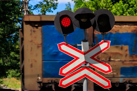 Red signal of semaphore and stop sign in front of railroad crossing with train passingの写真素材