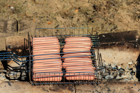 Grilling sausages in barbecue grill cooking on campfireの写真素材