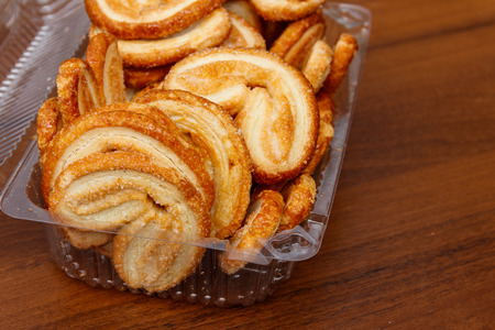 Palmier biscuits - french cookies made of puff pastry (also called palm leaves, elephant ears or french hearts) packed in plastic box on wooden tableの写真素材