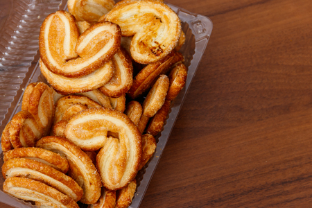 Palmier biscuits - french cookies made of puff pastry (also called palm leaves, elephant ears or french hearts) packed in plastic box on wooden table. Top viewの写真素材