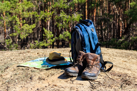 Tourist backpack with hiking boots, hat, compass and map on the glade in pine forest. Trekking hike gear equipment. Travel conceptの写真素材