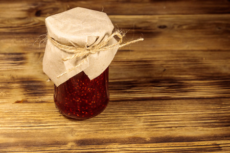 Raspberry jam in glass jar on wooden table