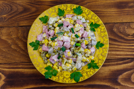 Tasty salad with sausage, green pea, canned corn, bell pepper, cucumber and mayonnaise on wooden tableの写真素材