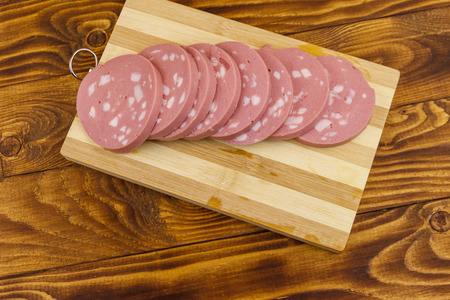 Sliced boiled sausage on cutting board on wooden tableの写真素材
