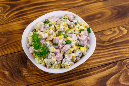 Tasty salad with sausage, green pea, canned corn, bell pepper, cucumber and mayonnaise on wooden tableの写真素材