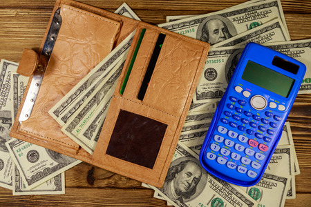 Opened wallet, calculator and american dollars banknotes on wooden table. Top view