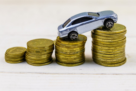 Miniature car model on stacks of golden coins on  white wooden backgroundの写真素材
