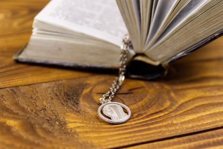 Open Holy Bible with Virgin Mary pendant on wooden backgroundの写真素材