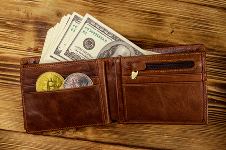 Wallet with american hundred dollars bills and bitcoins on wooden backgroundの写真素材