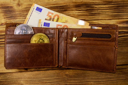 Wallet with fifty euro bills and bitcoins on wooden backgroundの写真素材