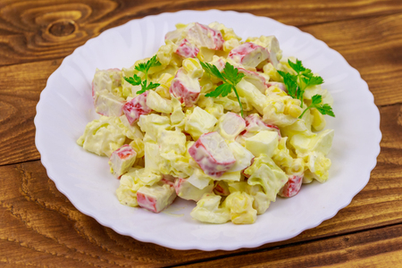 Salad with crab sticks, sweet corn, chinese cabbage, eggs and mayonnaise on wooden tableの写真素材