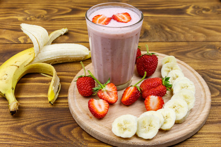 Glass of fresh smoothie of strawberry and banana on a wooden tableの写真素材