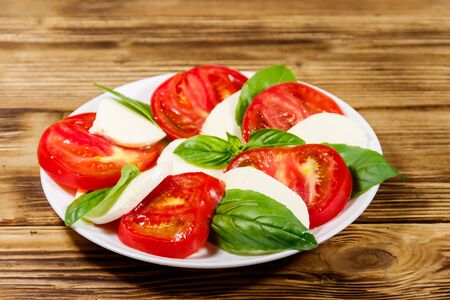 Italian caprese salad with tomatoes, mozzarella cheese and basil on a wooden tableの写真素材
