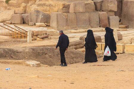 Cairo, Egypt - December 8, 2018: Arab with his two wives walking near Great pyramids of Giza in...