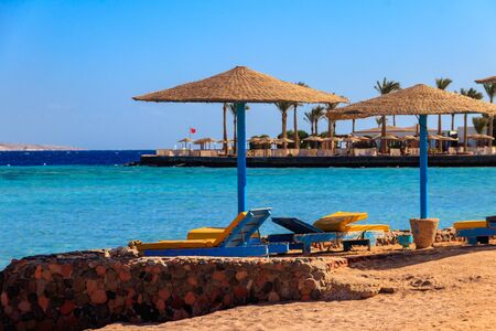 Sun umbrellas and chaise lounges on tropical beach. Concept of rest, relaxation, holidays, resortの写真素材