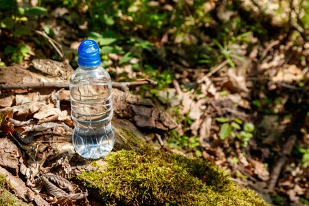 Plastic bottle with fresh drinking water on green forest backgroundの写真素材