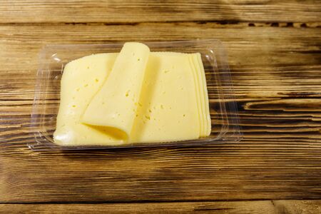 Slices of cheese in disposable plastic packing box on wooden table
