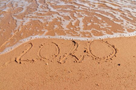 Concept of Christmas and New Year's holidays at tropical resort. 2020 number written on wet sand of...