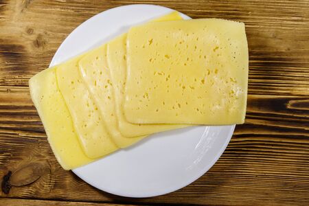 Slices of cheese in a plate on wooden table. Top view
