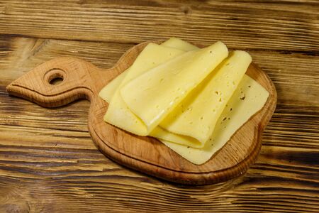 Slices of cheese on cutting board on wooden table