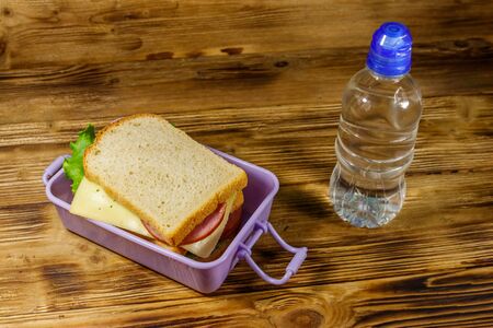 Lunch box with sandwiches and bottle of water on a wooden tableの写真素材