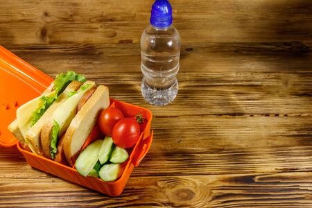 Bottle of water and lunch box with sandwiches and fresh vegetables on a wooden tableの写真素材