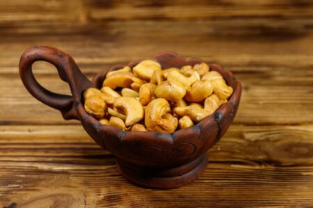 Ceramic bowl with roasted cashew nuts on a wooden tableの写真素材