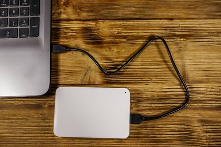External HDD connected to laptop computer on a wooden desk. Top view. Concept of data storageの写真素材
