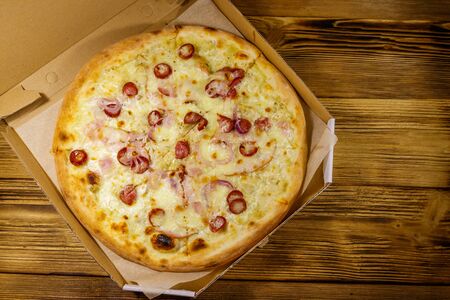 Delicious fresh pizza in cardboard box on a wooden table. Top view. Concept for home delivery of food, fast food, delivery of pizzaの写真素材