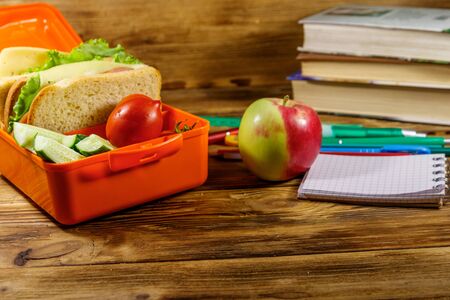 Back to school concept. School supplies, books, apple and lunch box with sandwiches and fresh vegetables on a wooden deskの写真素材