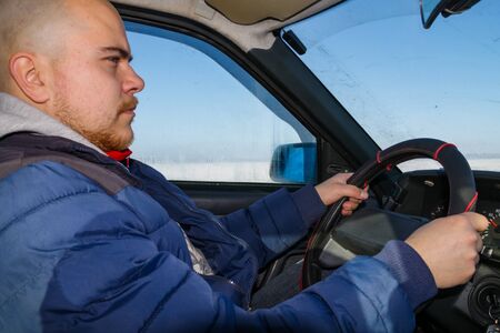 Young man driving a car on winter road. Inside view