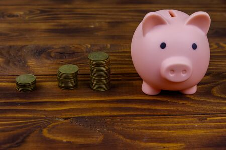 Pink piggy bank and coins on wooden background. Saving money concept