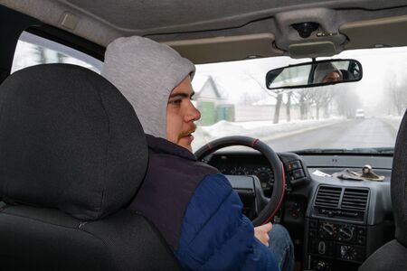 Young man driving a car on winter road. Inside view