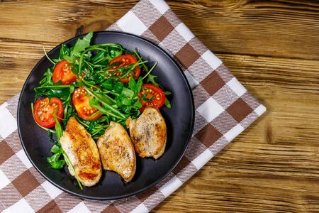 Fried chicken breast with salad of fresh arugula and cherry tomatoes on wooden table. Top viewの写真素材