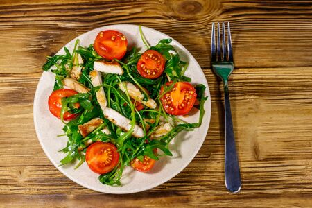 Tasty salad of fried chicken breast, fresh arugula and cherry tomatoes on wooden table. Top viewの写真素材
