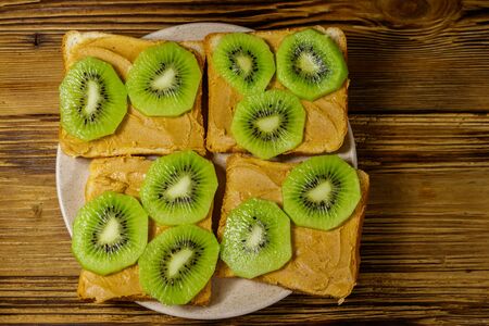 Tasty sandwiches with peanut butter and kiwi fruits on wooden table. Top viewの写真素材