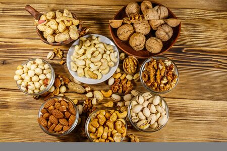 Assortment of nuts on wooden table. Almond, hazelnut, pistachio, peanut, walnut and cashew in small bowls. Top view. Healthy eating conceptの写真素材