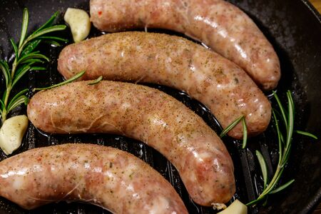 Raw sausages ready for preparation with rosemary, garlic and spices in cast iron grill frying panの写真素材