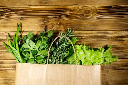 Paper bag with green onion, rosemary, lettuce leaves and parsley on wooden table. Top view. Healthy food and grocery shopping conceptの写真素材