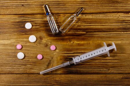 Concept of a prevention and treatment coronavirus. Pills, syringe, ampoules on a wooden background.の写真素材