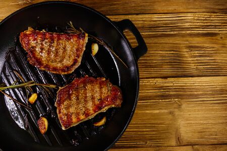 Grilled pork steaks with rosemary, garlic and spices in cast iron grill frying pan on wooden table. Top viewの写真素材