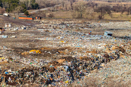 Horishni Plavni, Ukraine - February 29, 2020: Poor people collecting garbage at city garbage dump. Pile of plastic trash, food waste on landfill. Concept of poverty and environmental pollutionのeditorial素材