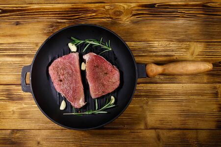 Raw pork steaks ready for preparation with rosemary, garlic and spices in cast iron grill frying pan on wooden table. Top viewの写真素材