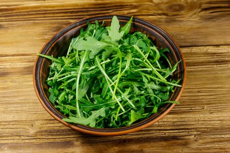 Fresh green arugula in ceramic bowl on a wooden table. Healthy food or vegetarian conceptの写真素材