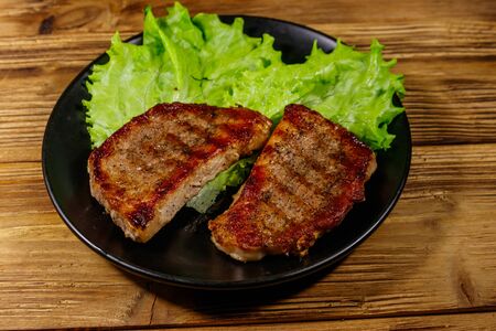 Grilled pork steaks with lettuce leaves on wooden table