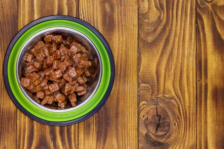 Canned food for cats or dogs in green metal bowl on wooden floor. Top viewの写真素材