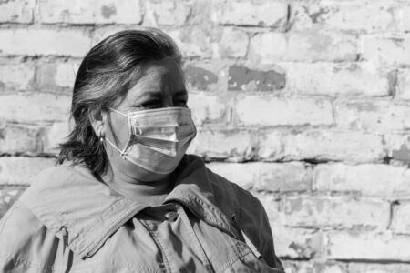 Senior woman stands in a medical mask on her face, which protects against coronavirus and other...