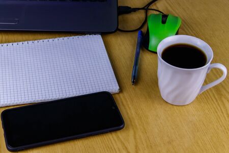 Laptop with mouse, smartphone, notebook, pen and cup of coffee on a desk. Working at home and business conceptの写真素材