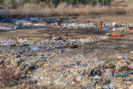 Horishni Plavni, Ukraine - February 29, 2020: Poor people collecting garbage at city garbage dump. Pile of plastic trash, food waste on landfill. Concept of poverty and environmental pollutionのeditorial素材
