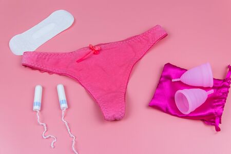 Women's panties with menstrual cups, sanitary pads and tampons on pastel pink background. Concept of...